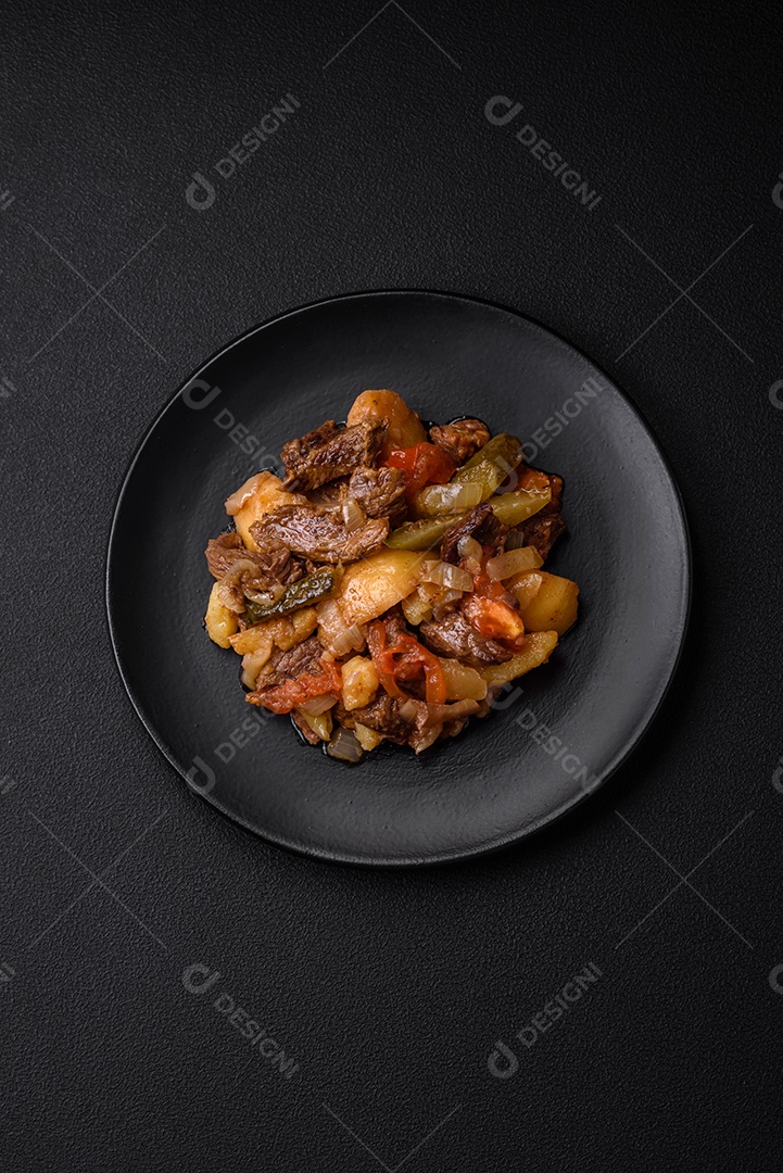 Delicioso ensopado com batatas, tomates, carne, cebolas e cenouras num prato cerâmico sobre um fundo escuro de concreto