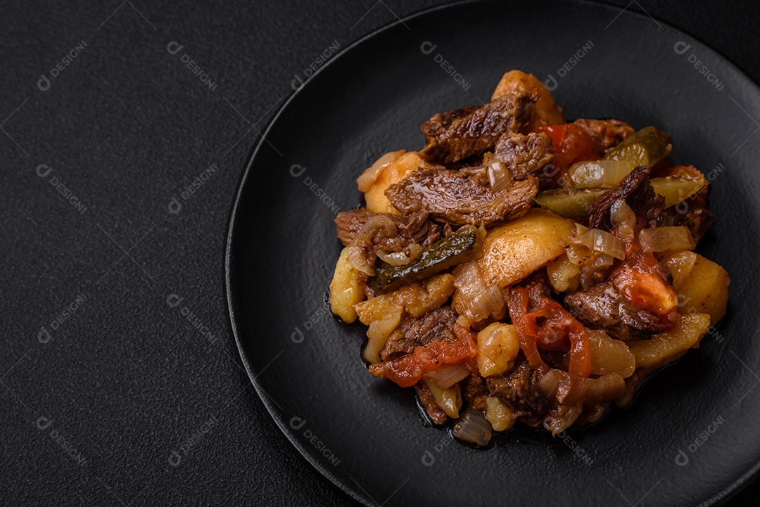 Delicioso ensopado com batatas, tomates, carne, cebolas e cenouras num prato cerâmico sobre um fundo escuro de concreto