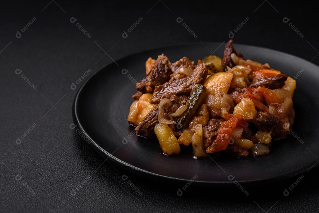 Delicioso ensopado com batatas, tomates, carne, cebolas e cenouras num prato cerâmico sobre um fundo escuro de concreto