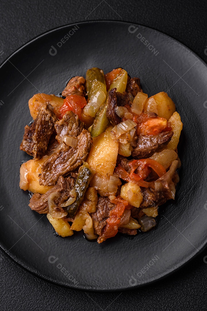 Delicioso ensopado com batatas, tomates, carne, cebolas e cenouras num prato cerâmico sobre um fundo escuro de concreto