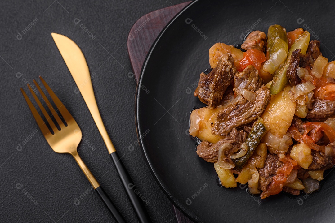 Delicioso ensopado com batatas, tomates, carne, cebolas e cenouras num prato cerâmico sobre um fundo escuro de concreto