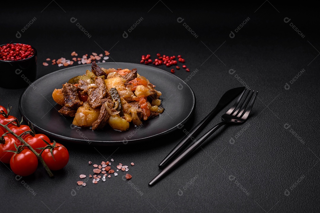 Delicioso ensopado com batatas, tomates, carne, cebolas e cenouras num prato cerâmico sobre um fundo escuro de concreto