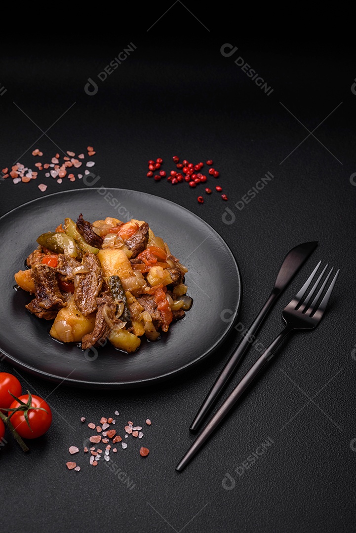 Delicioso ensopado com batatas, tomates, carne, cebolas e cenouras num prato cerâmico sobre um fundo escuro de concreto
