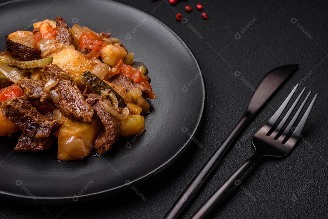 Delicioso ensopado com batatas, tomates, carne, cebolas e cenouras num prato cerâmico sobre um fundo escuro de concreto