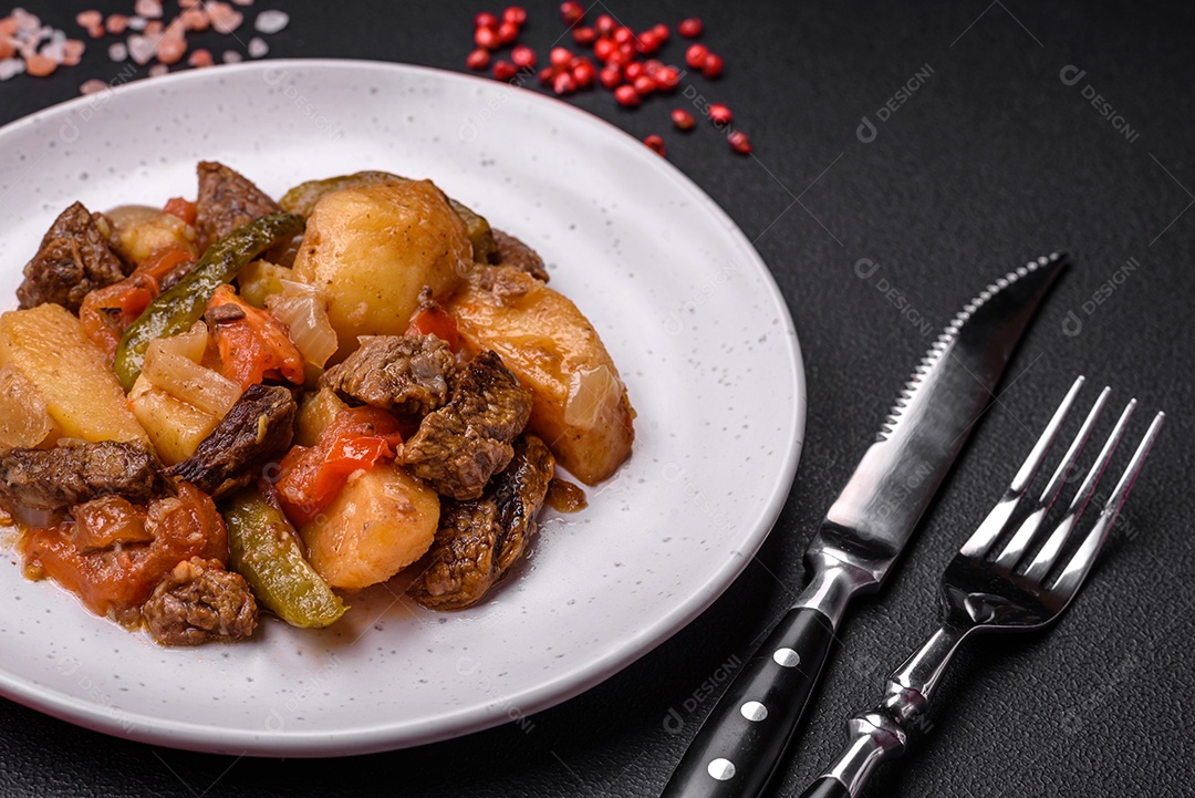 Delicioso ensopado com batatas, tomates, carne, cebolas e cenouras num prato cerâmico sobre um fundo escuro de concreto