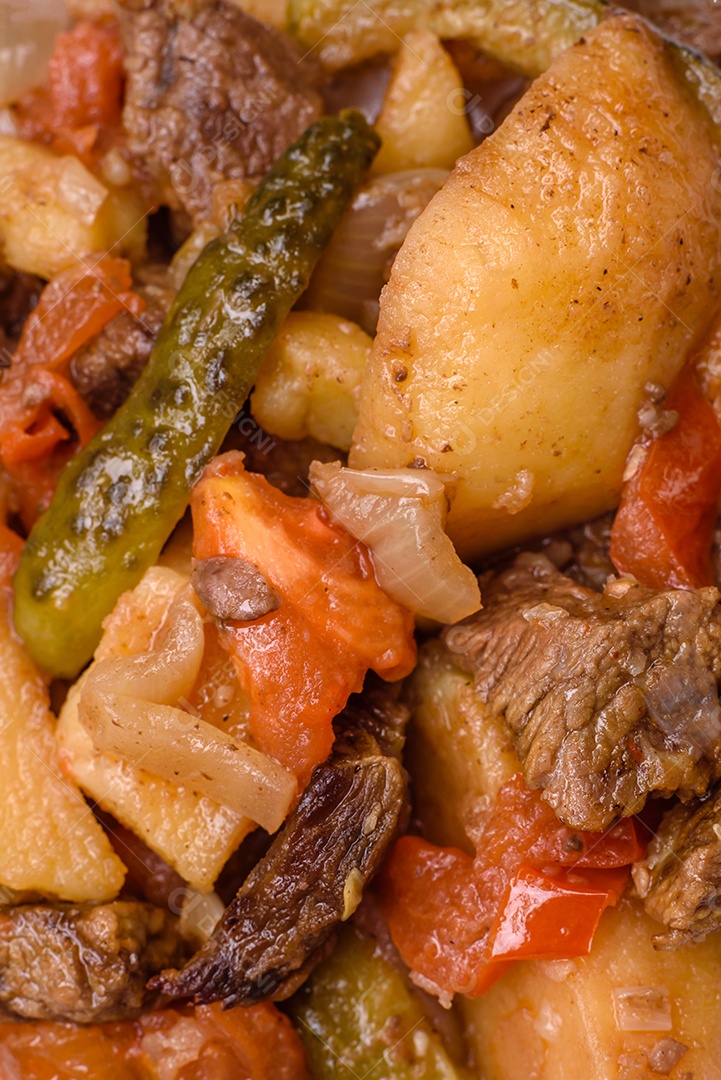 Delicioso ensopado com batatas, tomates, carne, cebolas e cenouras num prato cerâmico sobre um fundo escuro de concreto