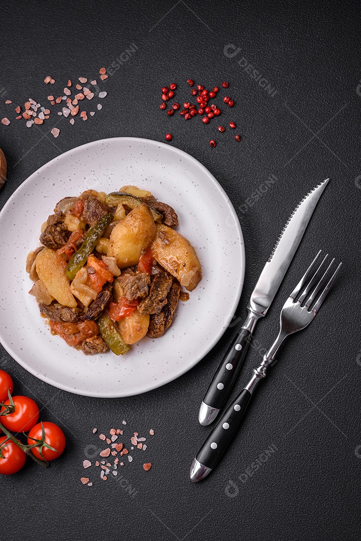 Delicioso ensopado com batatas, tomates, carne, cebolas e cenouras num prato cerâmico sobre um fundo escuro de concreto