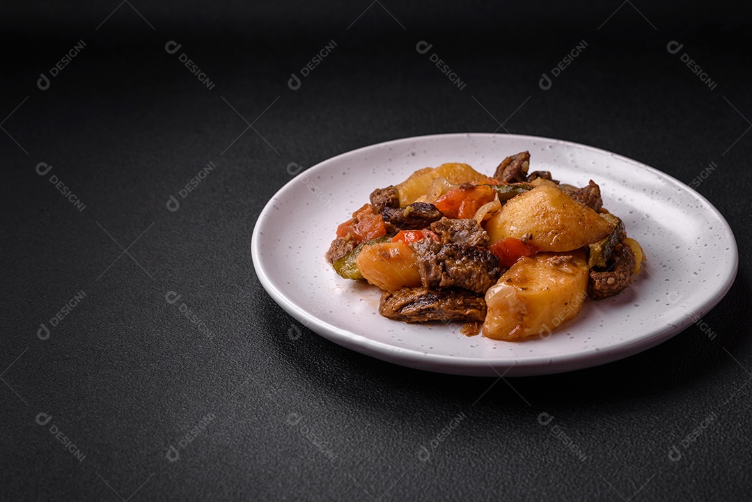 Delicioso ensopado com batatas, tomates, carne, cebolas e cenouras num prato cerâmico sobre um fundo escuro de concreto