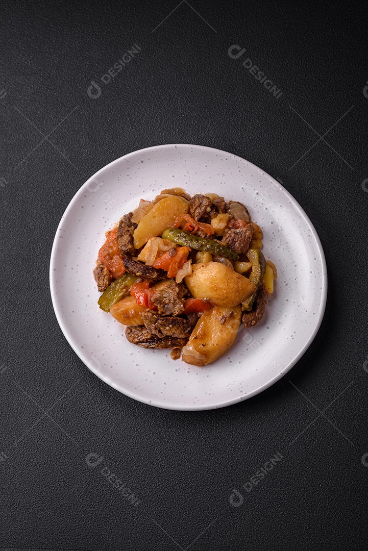 Delicioso ensopado com batatas, tomates, carne, cebolas e cenouras num prato cerâmico sobre um fundo escuro de concreto