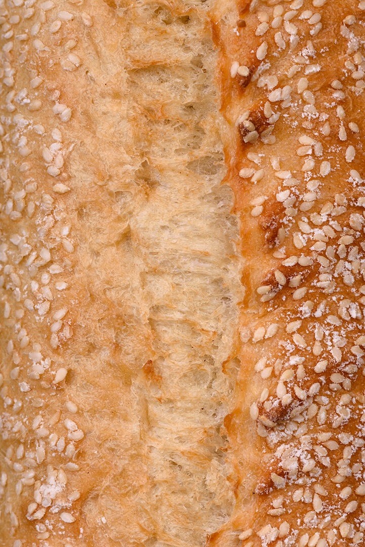 Baguete de farinha de trigo crocante com sementes de gergelim em uma tábua de madeira sobre um fundo escuro de concreto