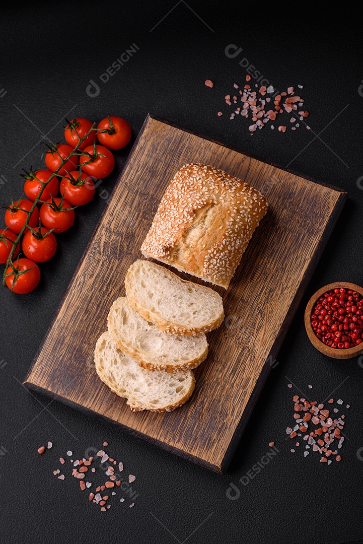 Baguete de farinha de trigo crocante com sementes de gergelim em uma tábua de madeira sobre um fundo escuro de concreto