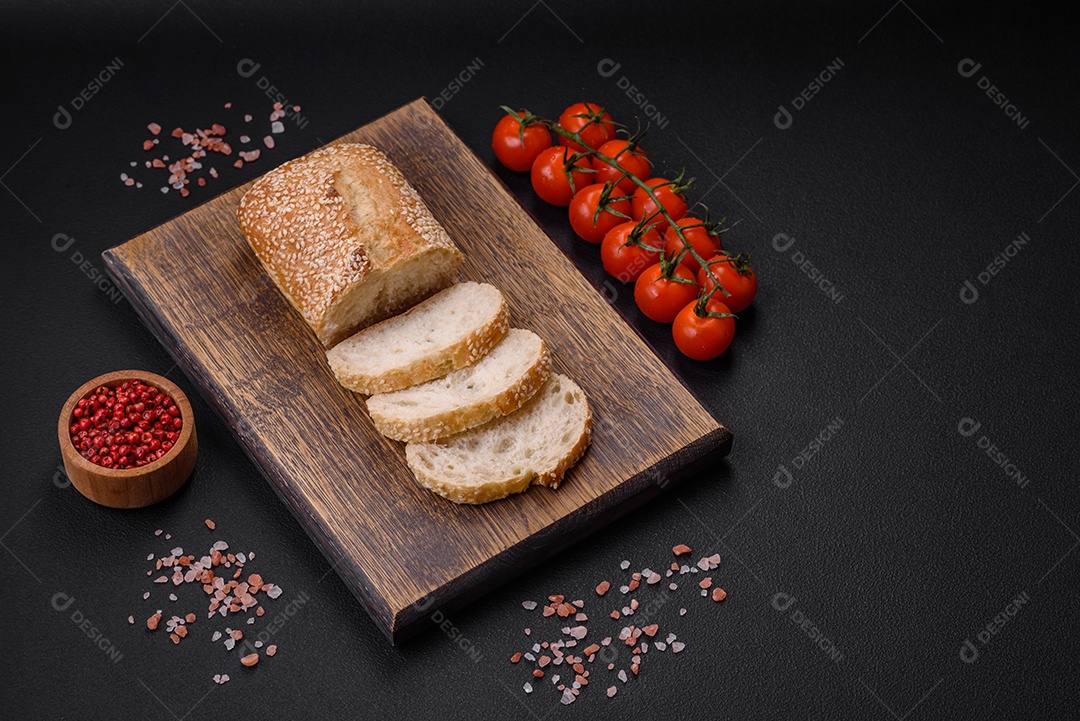 Baguete de farinha de trigo crocante com sementes de gergelim em uma tábua de madeira sobre um fundo escuro de concreto
