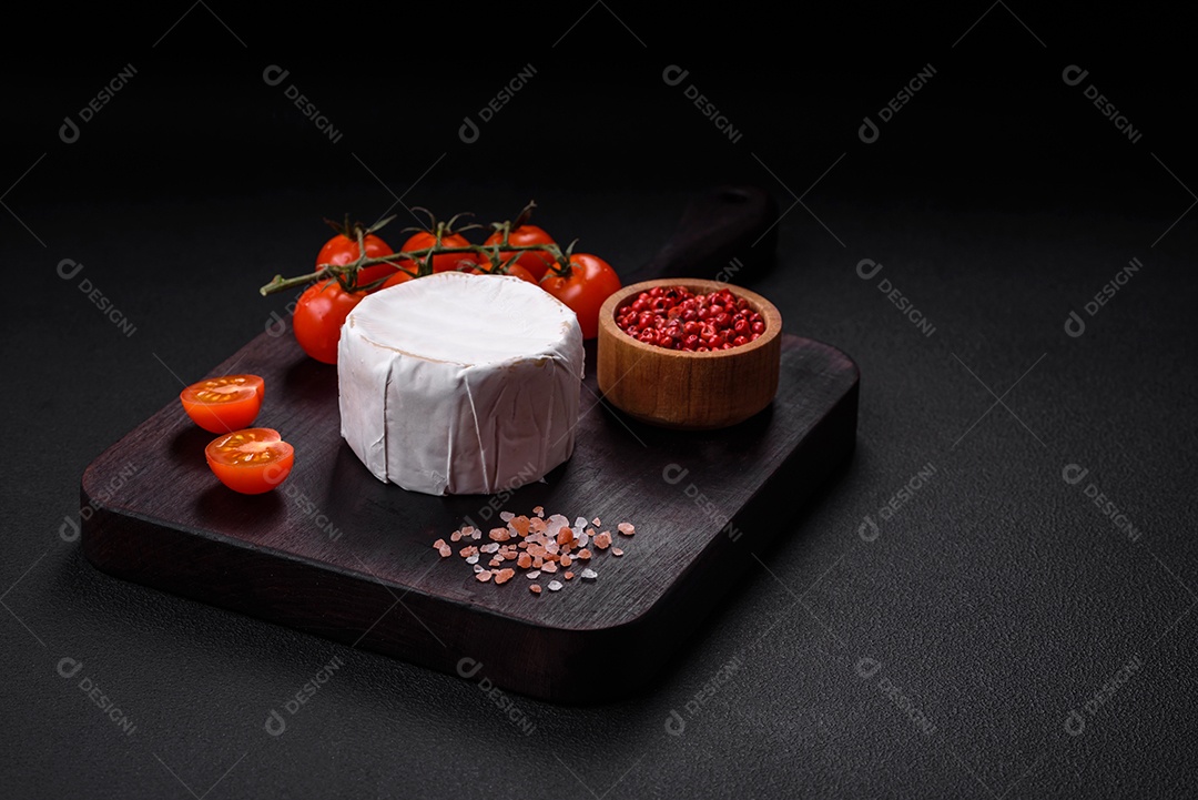 Delicioso queijo brie fresco em forma de mini cabeça com tomate cereja sobre fundo escuro de concreto
