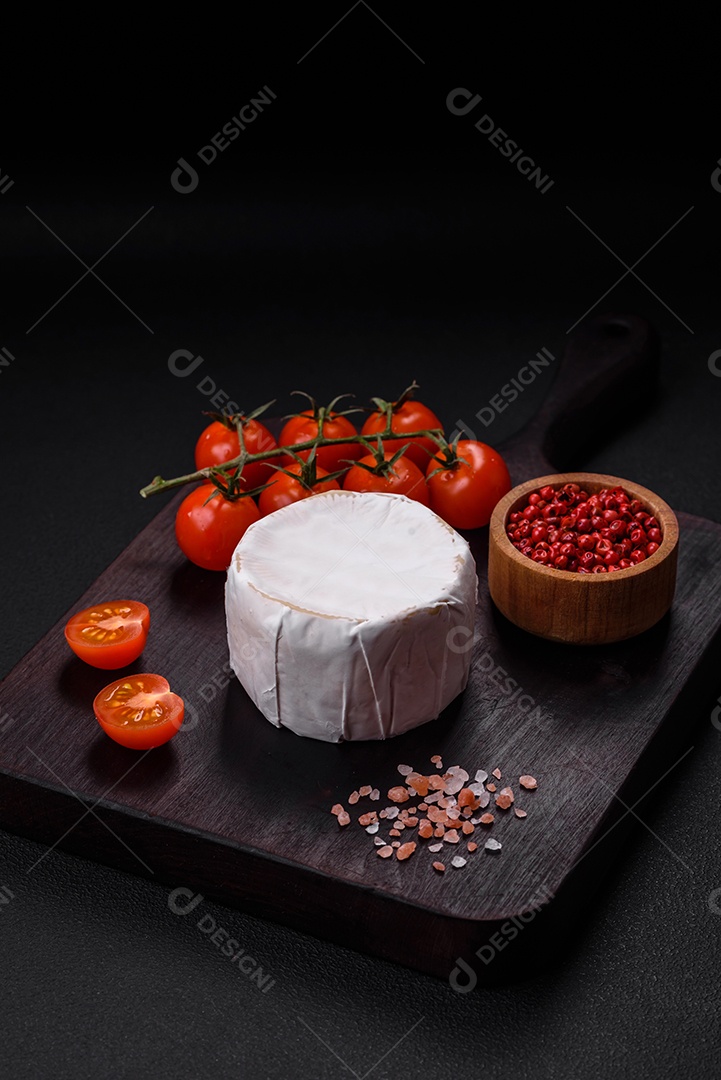 Delicioso queijo brie fresco em forma de mini cabeça com tomate cereja sobre fundo escuro de concreto