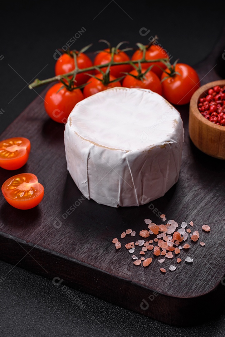 Delicioso queijo brie fresco em forma de mini cabeça com tomate cereja sobre fundo escuro de concreto