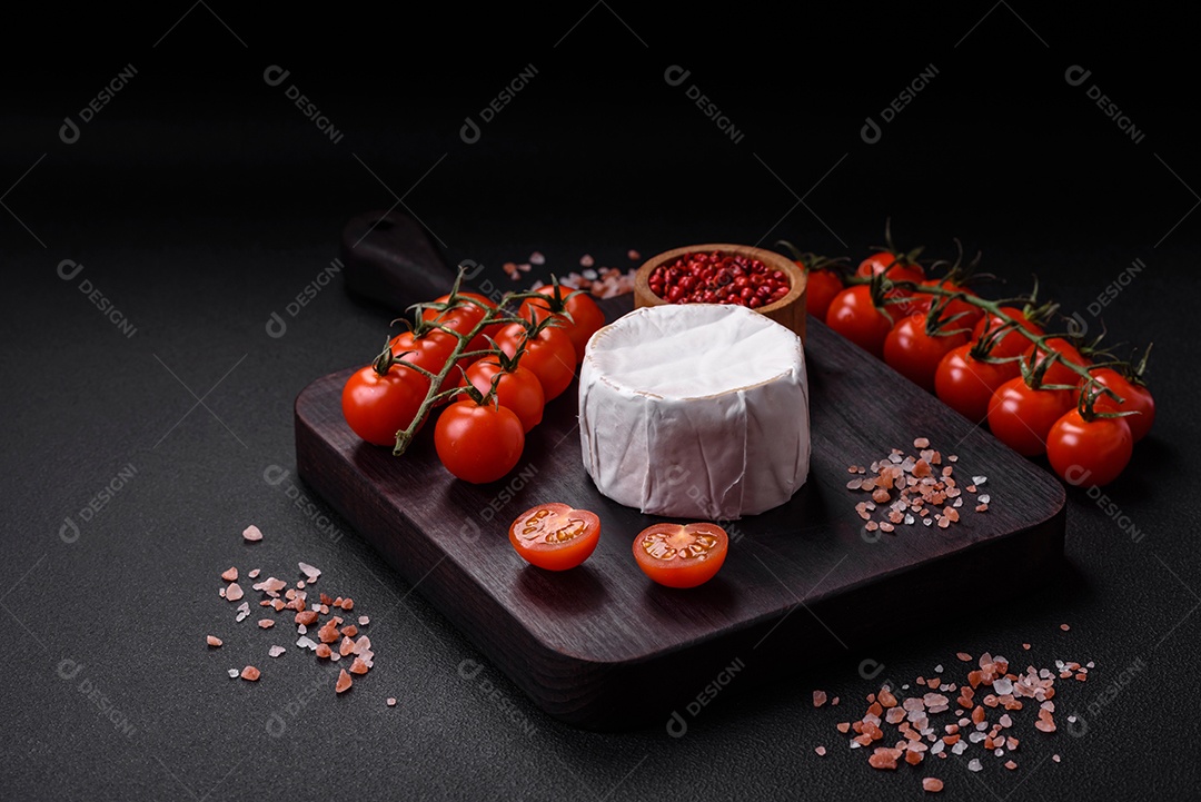 Delicioso queijo brie fresco em forma de mini cabeça com tomate cereja sobre fundo escuro de concreto