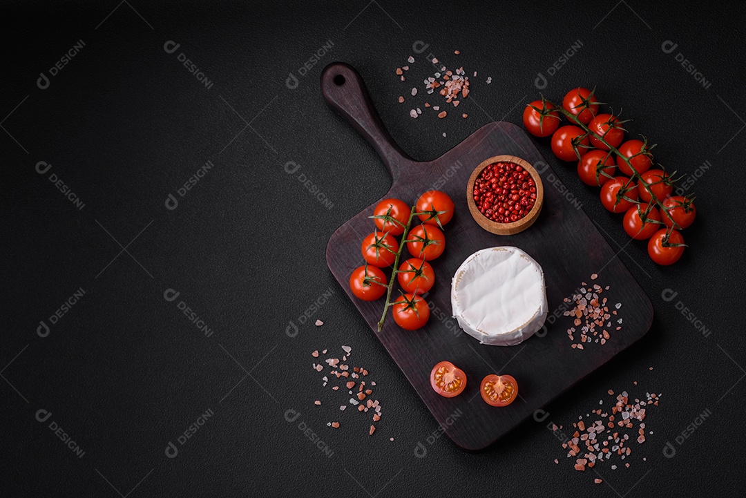 Delicioso queijo brie fresco em forma de mini cabeça com tomate cereja sobre fundo escuro de concreto