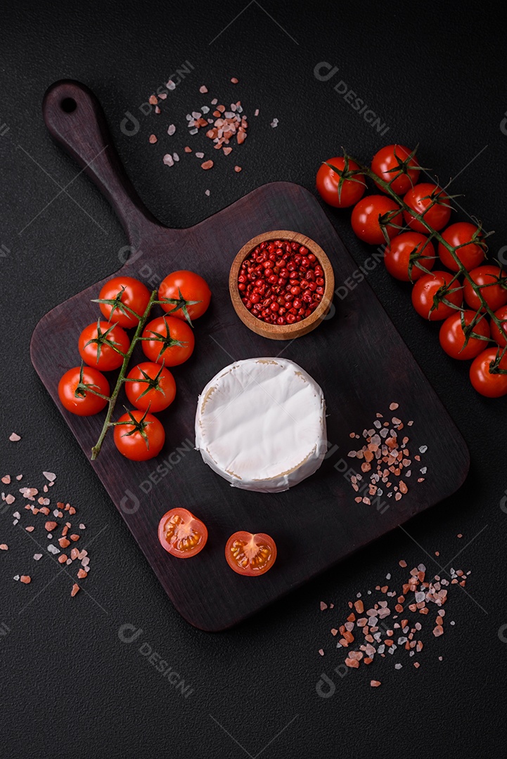 Delicioso queijo brie fresco em forma de mini cabeça com tomate cereja sobre fundo escuro de concreto