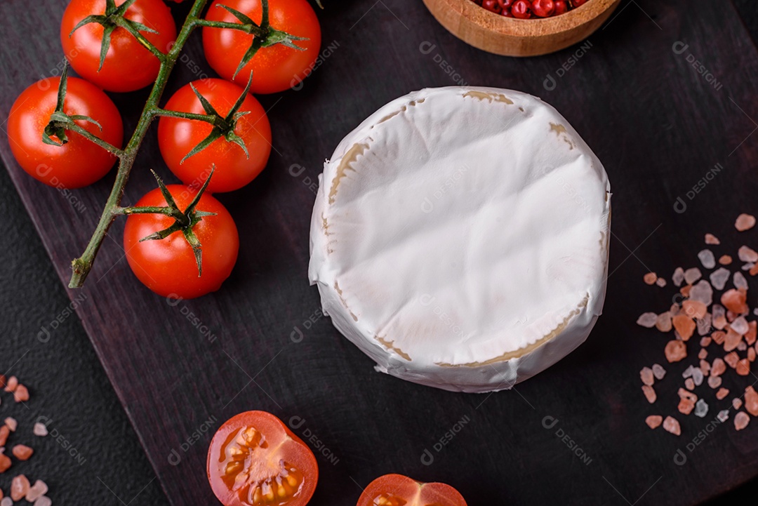 Delicioso queijo brie fresco em forma de mini cabeça com tomate cereja sobre fundo escuro de concreto