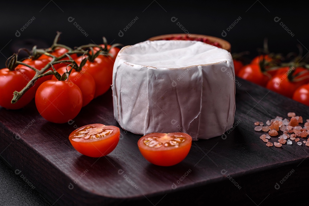 Delicioso queijo brie fresco em forma de mini cabeça com tomate cereja sobre fundo escuro de concreto