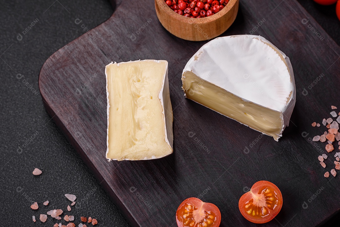 Delicioso queijo brie fresco em forma de mini cabeça com tomate cereja sobre fundo escuro de concreto