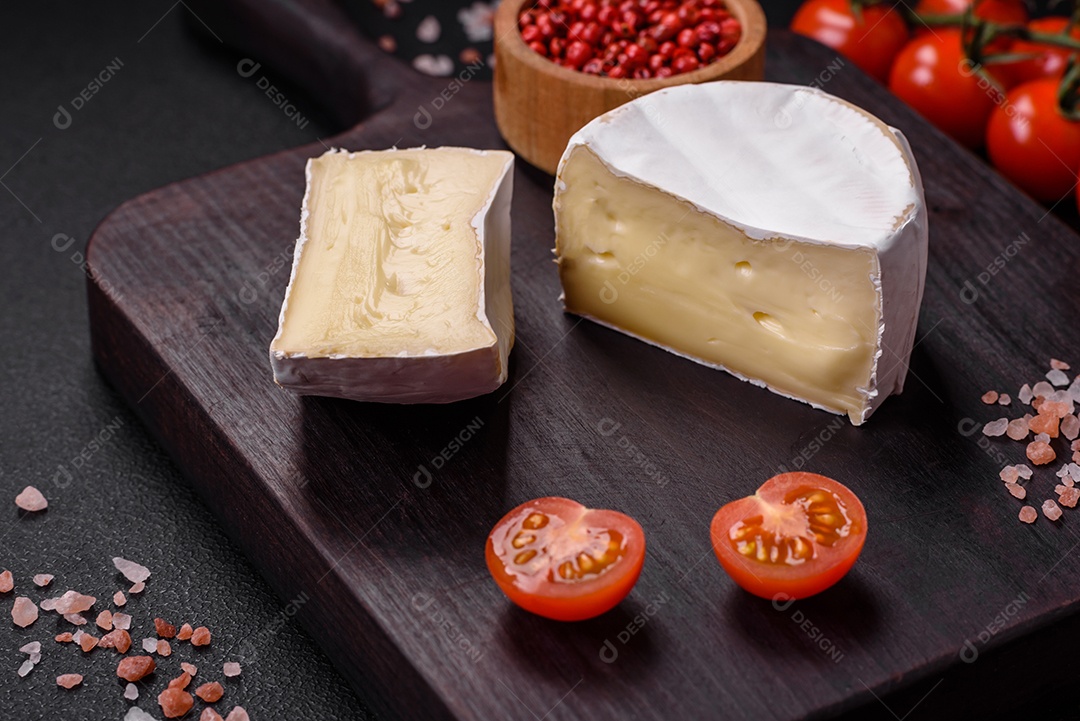 Delicioso queijo brie fresco em forma de mini cabeça com tomate cereja sobre fundo escuro de concreto
