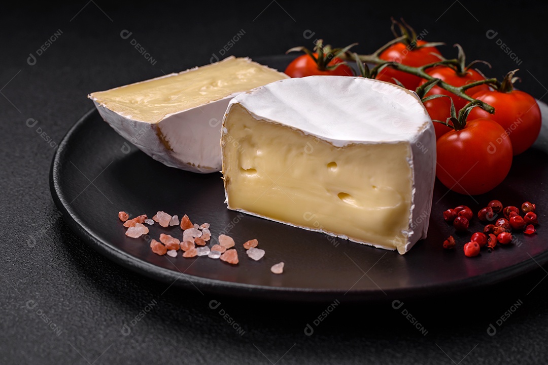 Delicioso queijo brie fresco em forma de mini cabeça com tomate cereja sobre fundo escuro de concreto