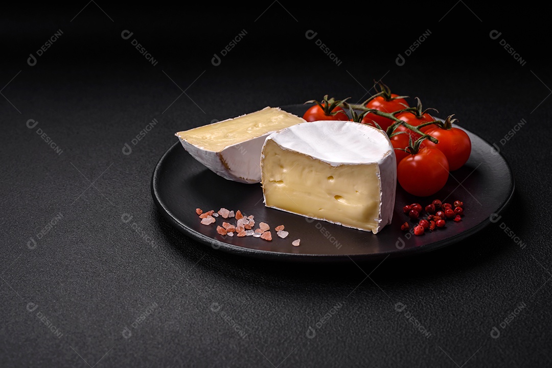 Delicioso queijo brie fresco em forma de mini cabeça com tomate cereja sobre fundo escuro de concreto