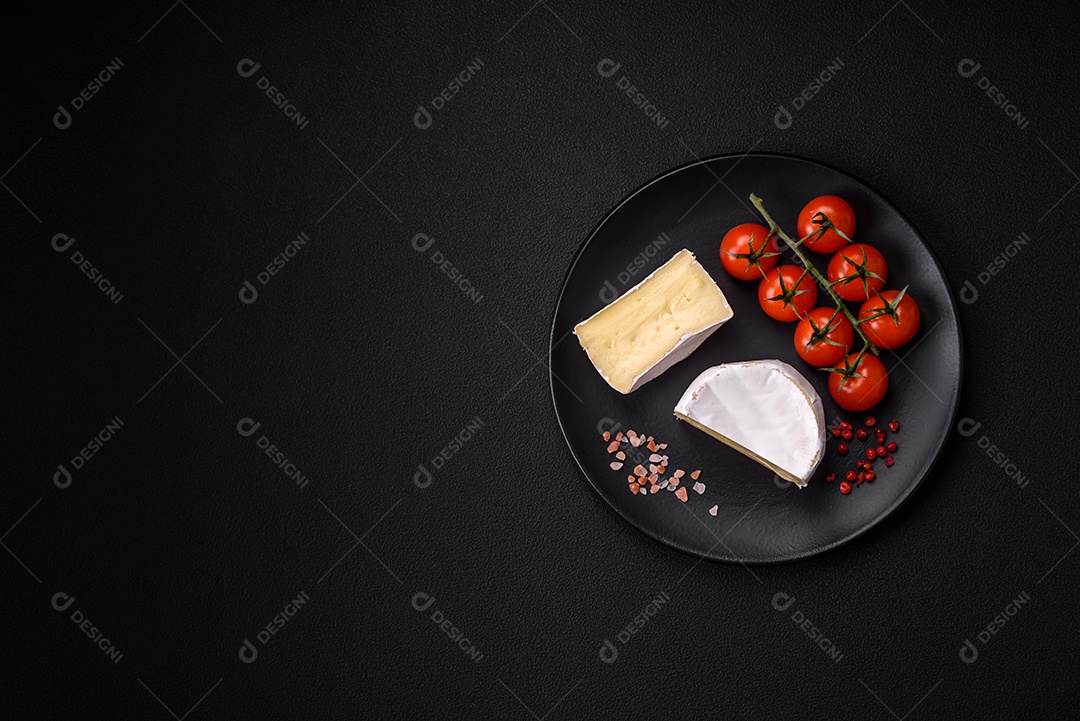 Delicioso queijo brie fresco em forma de mini cabeça com tomate cereja sobre fundo escuro de concreto