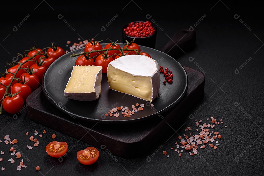 Delicioso queijo brie fresco em forma de mini cabeça com tomate cereja sobre fundo escuro de concreto