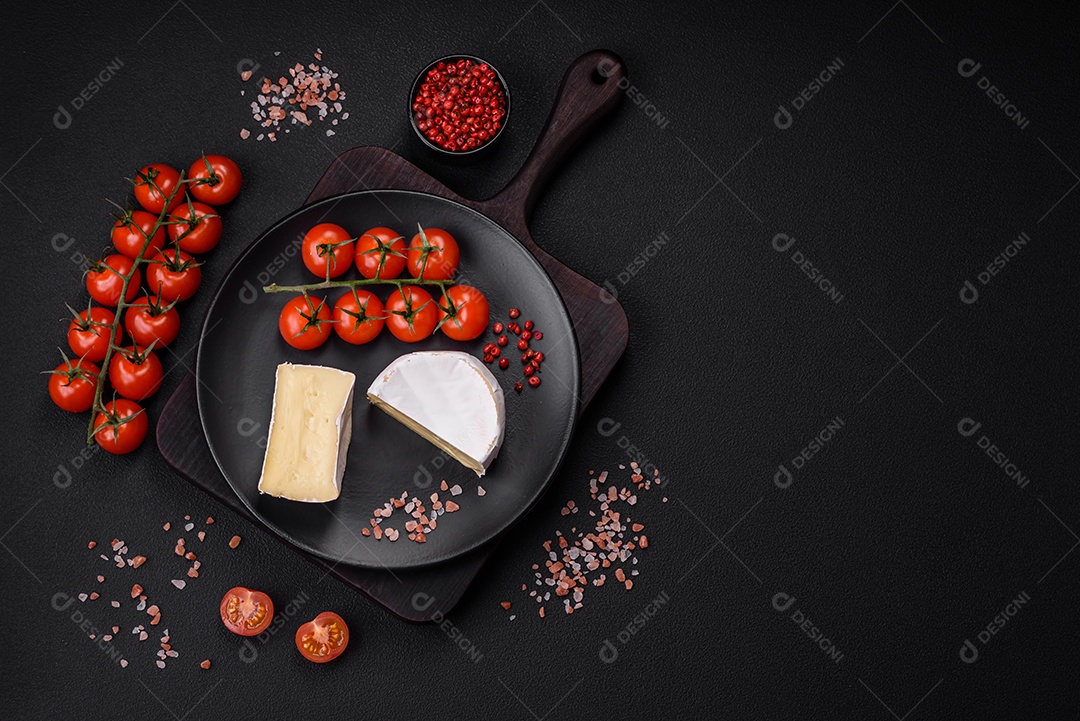 Delicioso queijo brie fresco em forma de mini cabeça com tomate cereja sobre fundo escuro de concreto