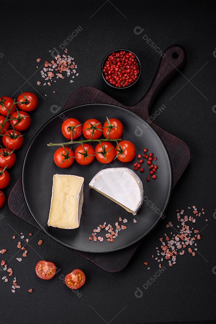 Delicioso queijo brie fresco em forma de mini cabeça com tomate cereja sobre fundo escuro de concreto