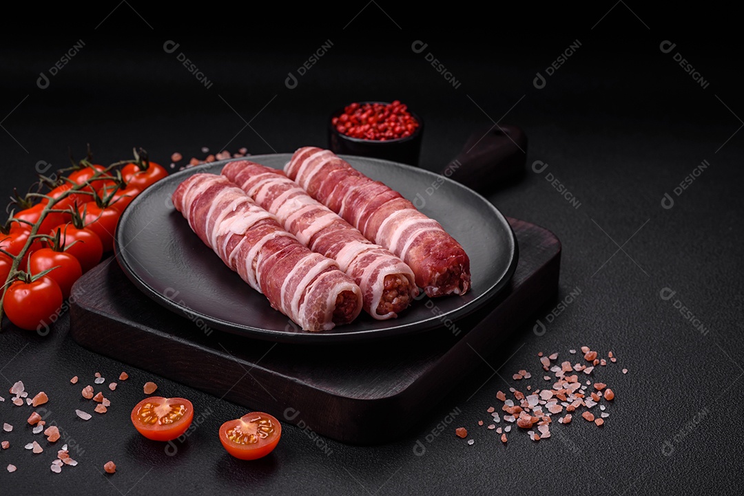 Carne picada crua embrulhada em bacon com sal e especiarias ou cevapcici sobre fundo escuro de concreto