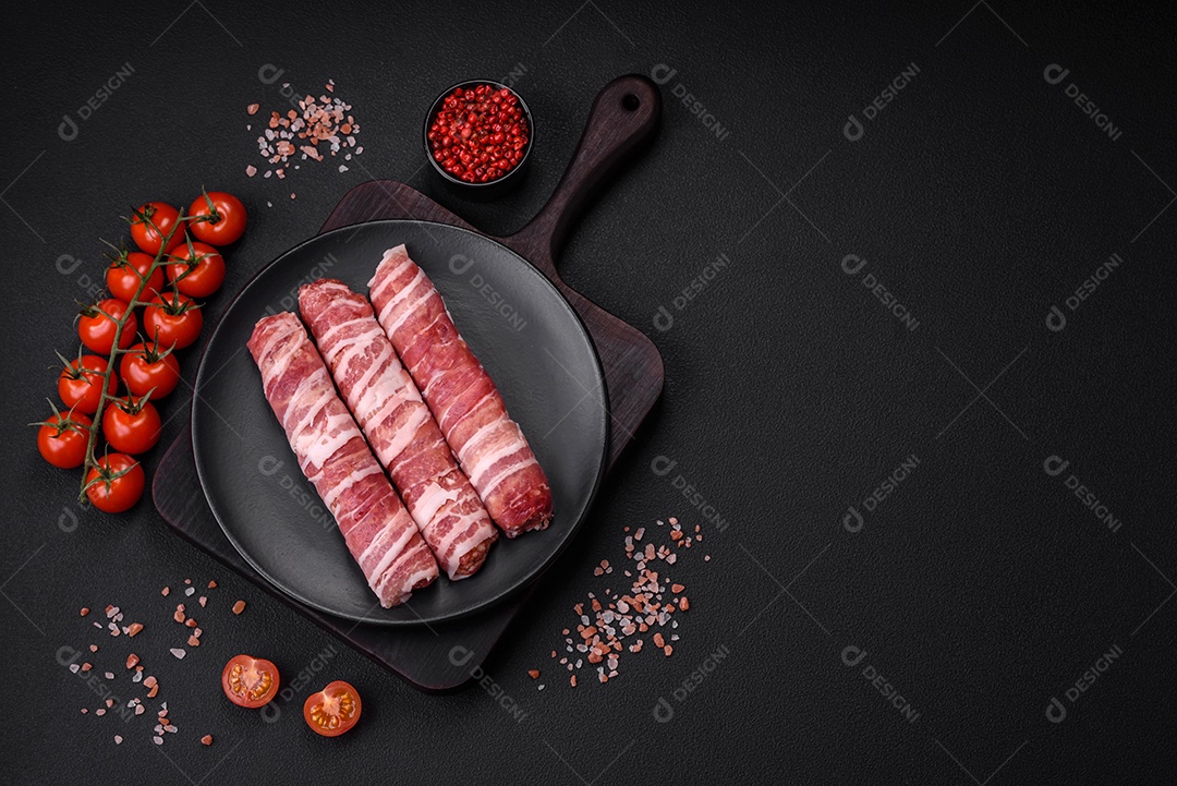 Carne picada crua embrulhada em bacon com sal e especiarias ou cevapcici sobre fundo escuro de concreto