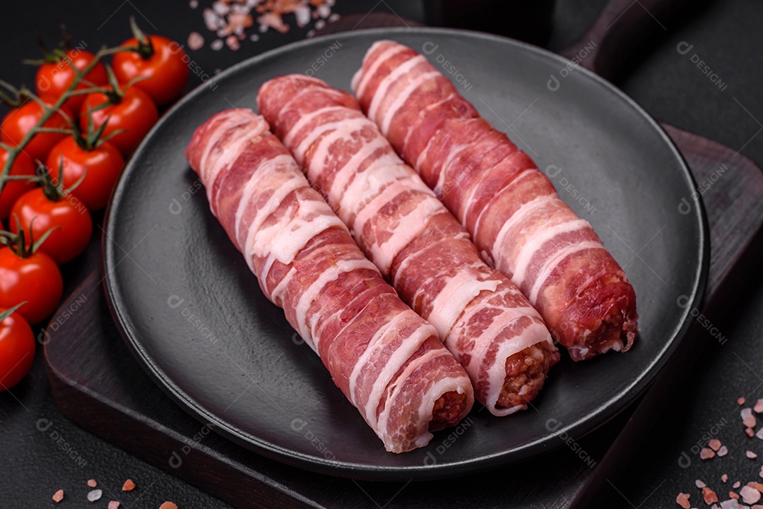 Carne picada crua embrulhada em bacon com sal e especiarias ou cevapcici sobre fundo escuro de concreto