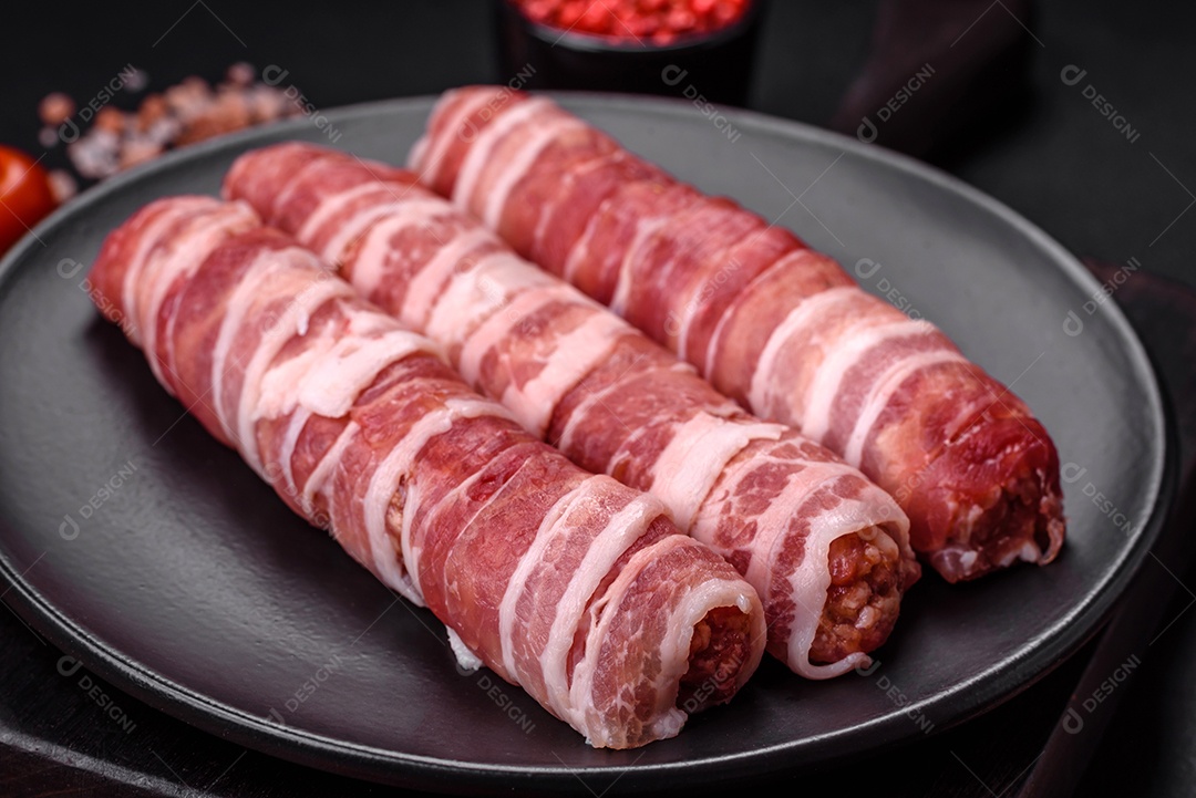 Carne picada crua embrulhada em bacon com sal e especiarias ou cevapcici sobre fundo escuro de concreto