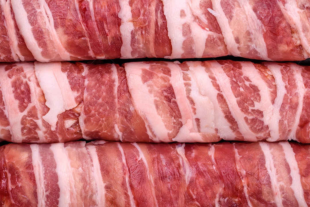 Carne picada crua embrulhada em bacon com sal e especiarias ou cevapcici sobre fundo escuro de concreto