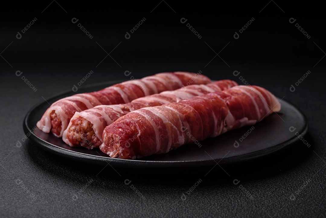 Carne picada crua embrulhada em bacon com sal e especiarias ou cevapcici sobre fundo escuro de concreto