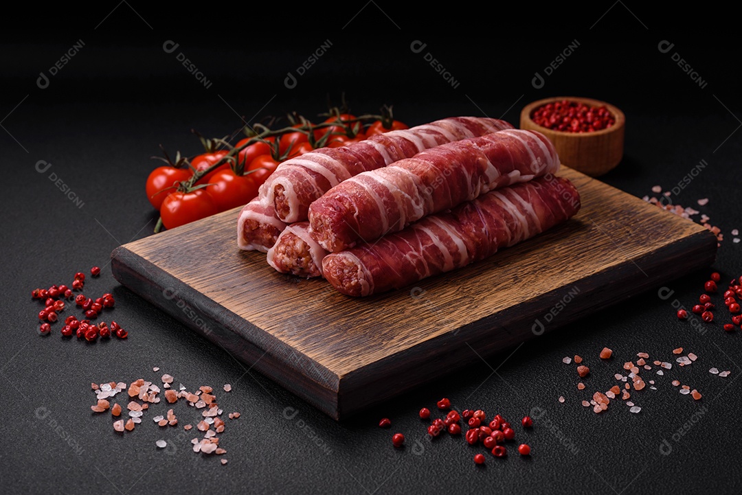 Carne picada crua embrulhada em bacon com sal e especiarias ou cevapcici sobre fundo escuro de concreto