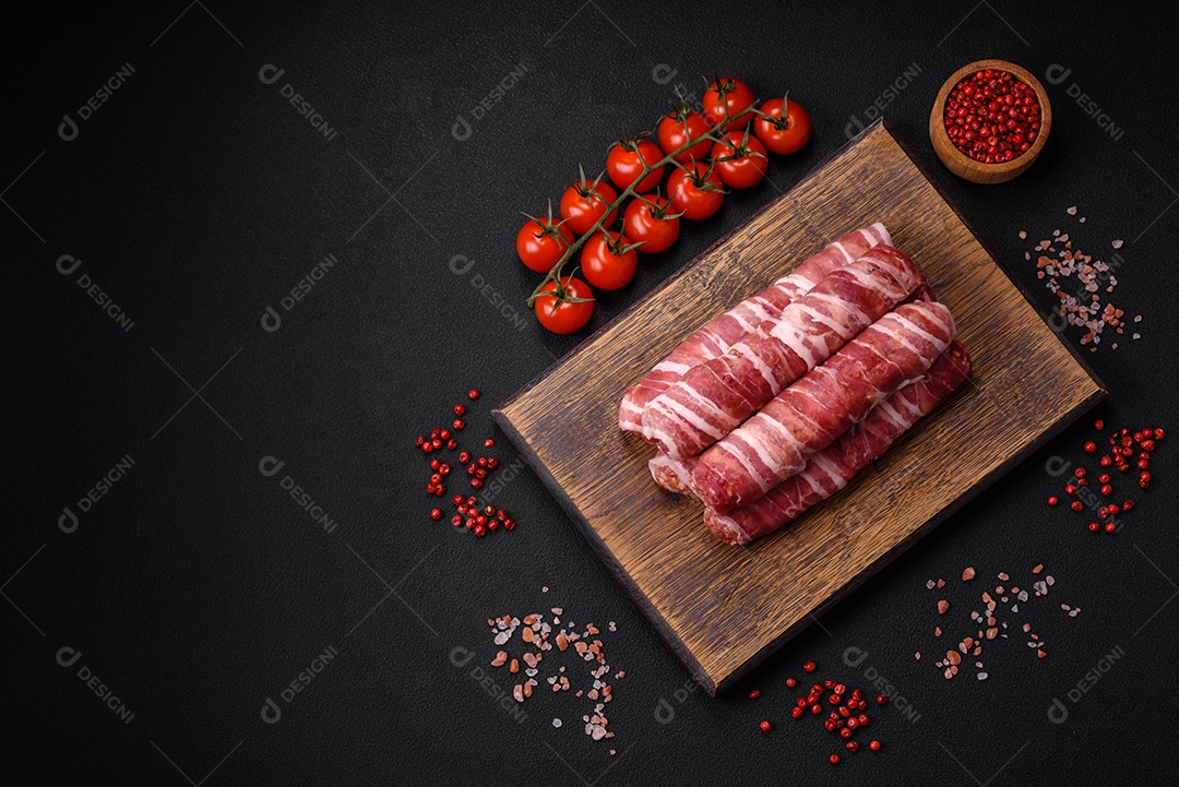 Carne picada crua embrulhada em bacon com sal e especiarias ou cevapcici sobre fundo escuro de concreto