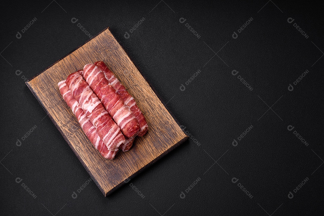 Carne picada crua embrulhada em bacon com sal e especiarias ou cevapcici sobre fundo escuro de concreto