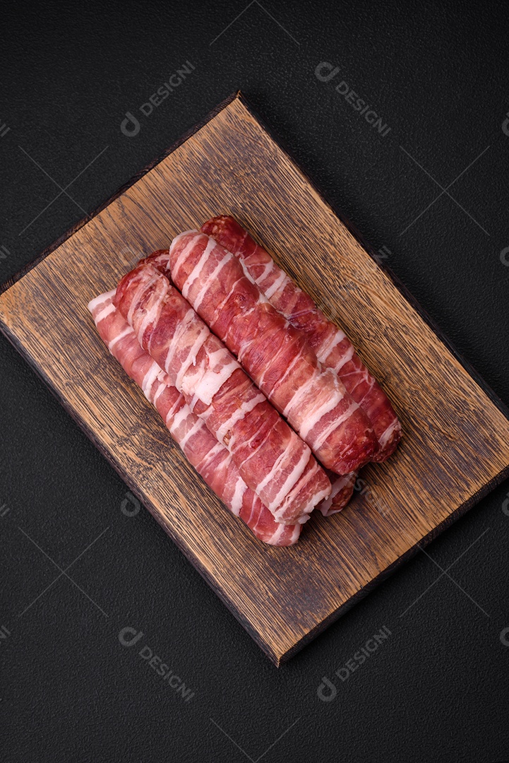 Carne picada crua embrulhada em bacon com sal e especiarias ou cevapcici sobre fundo escuro de concreto