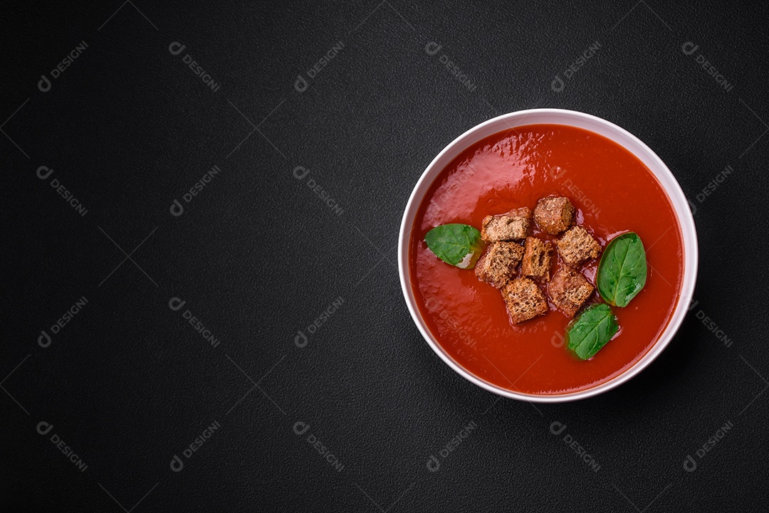 Delicioso gaspacho fresco com pão ralado, sal e especiarias numa placa cerâmica sobre um fundo escuro de concreto