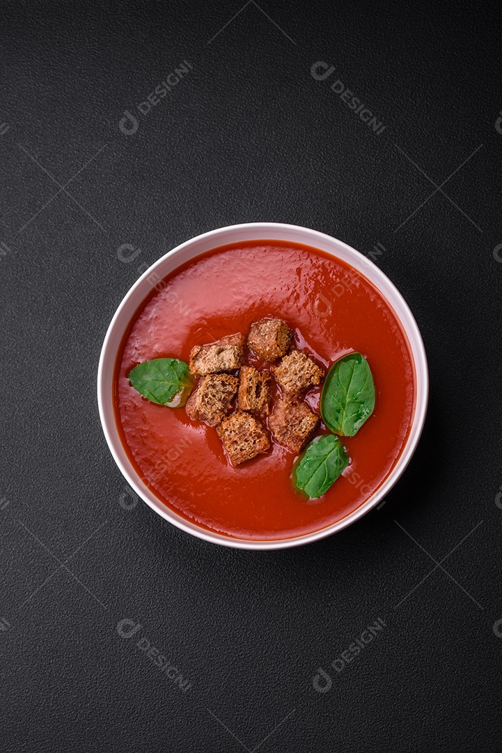 Delicioso gaspacho fresco com pão ralado, sal e especiarias numa placa cerâmica sobre um fundo escuro de concreto