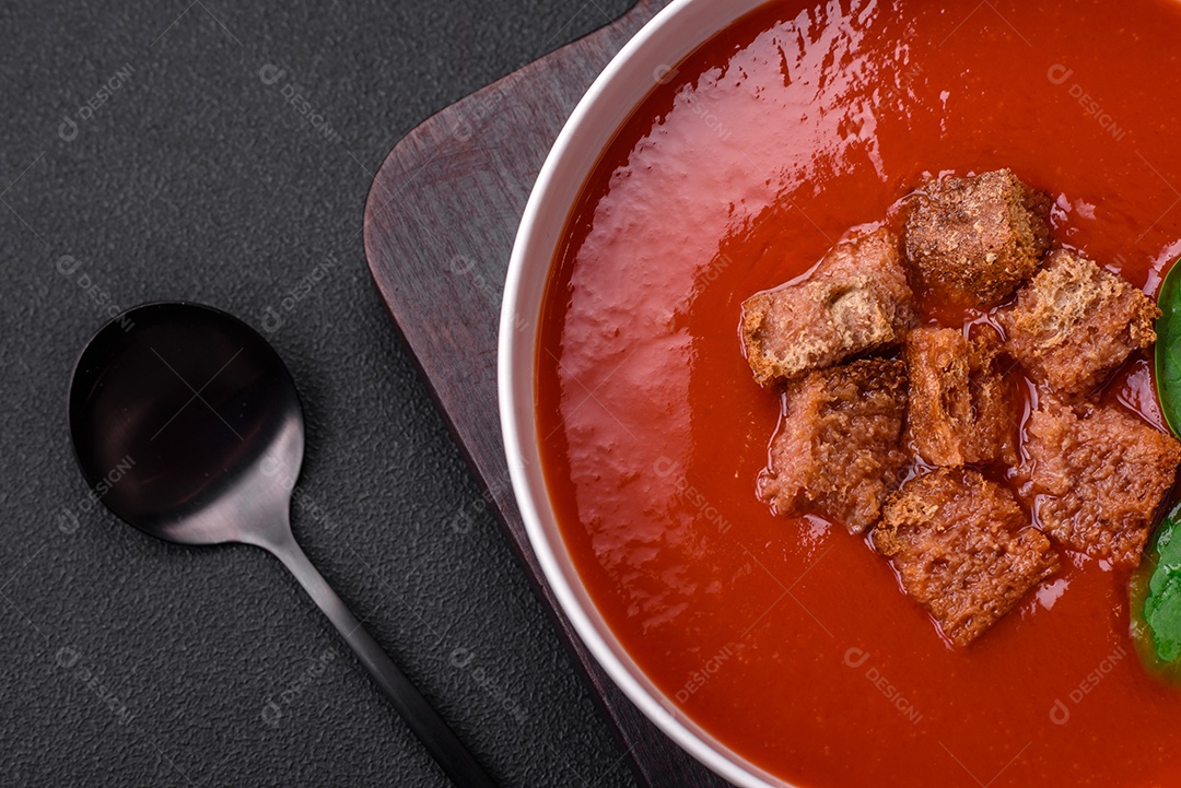 Delicioso gaspacho fresco com pão ralado, sal e especiarias numa placa cerâmica sobre um fundo escuro de concreto