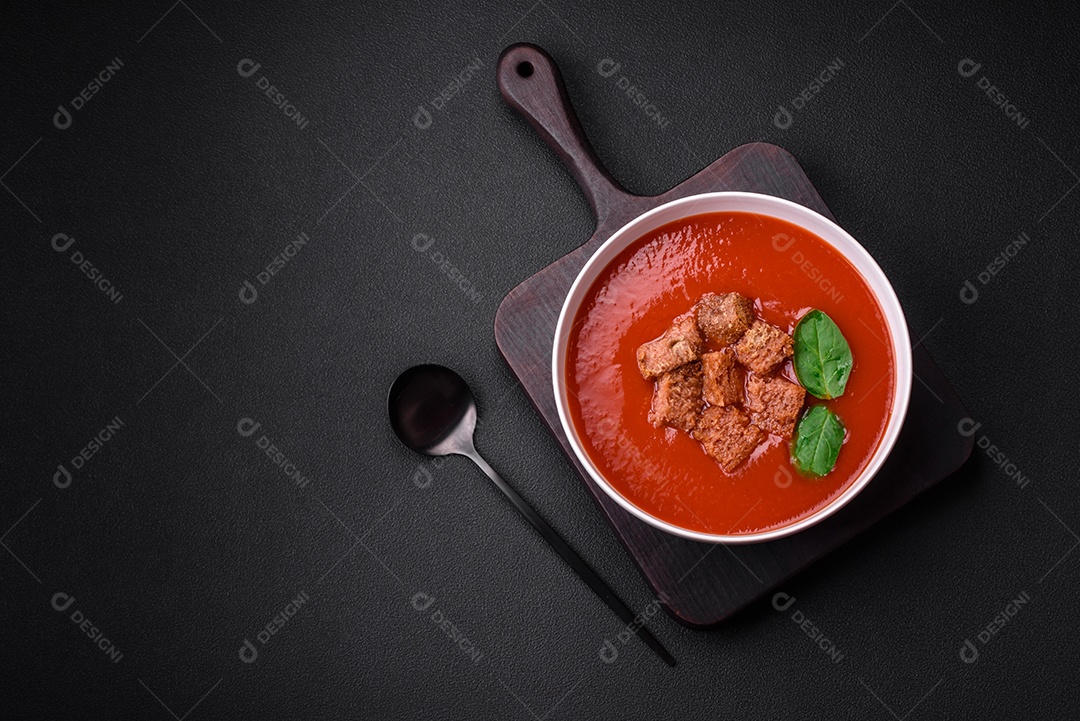 Delicioso gaspacho fresco com pão ralado, sal e especiarias numa placa cerâmica sobre um fundo escuro de concreto