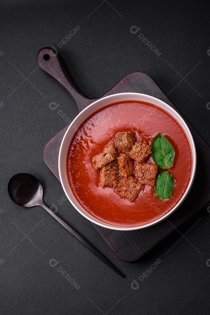 Delicioso gaspacho fresco com pão ralado, sal e especiarias numa placa cerâmica sobre um fundo escuro de concreto