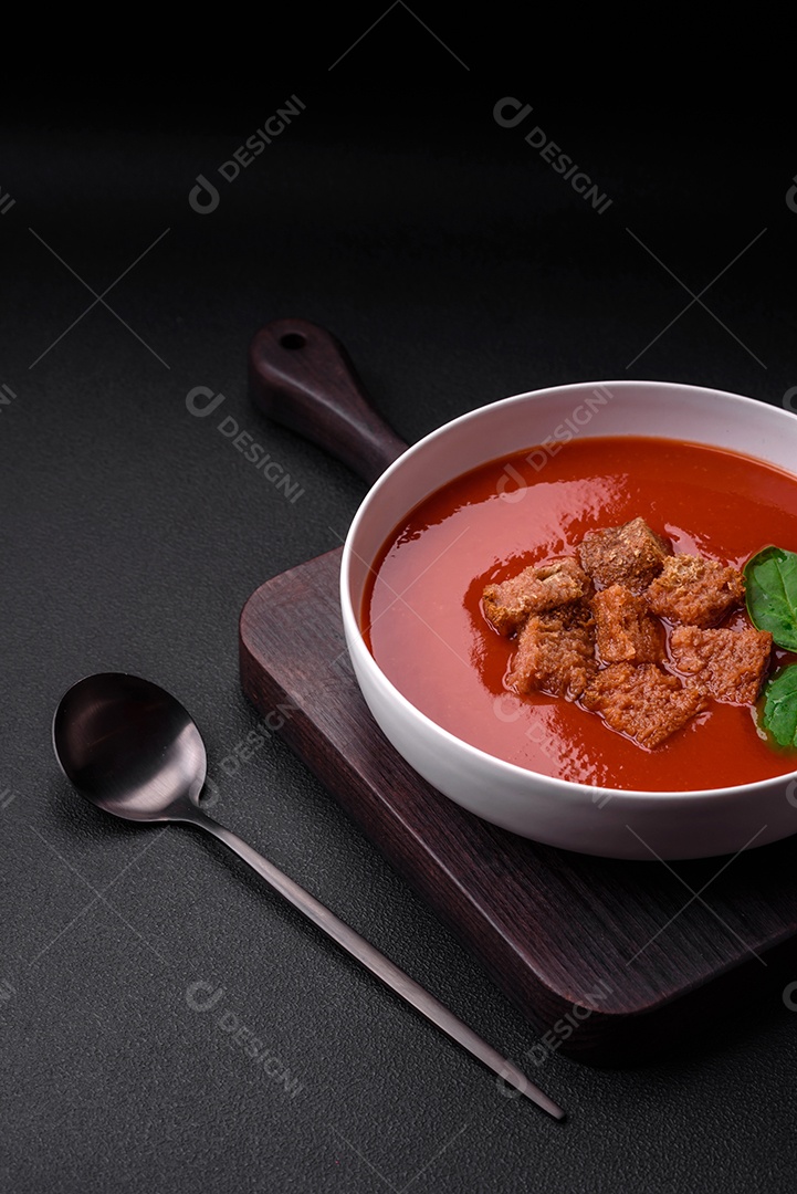 Delicioso gaspacho fresco com pão ralado, sal e especiarias numa placa cerâmica sobre um fundo escuro de concreto