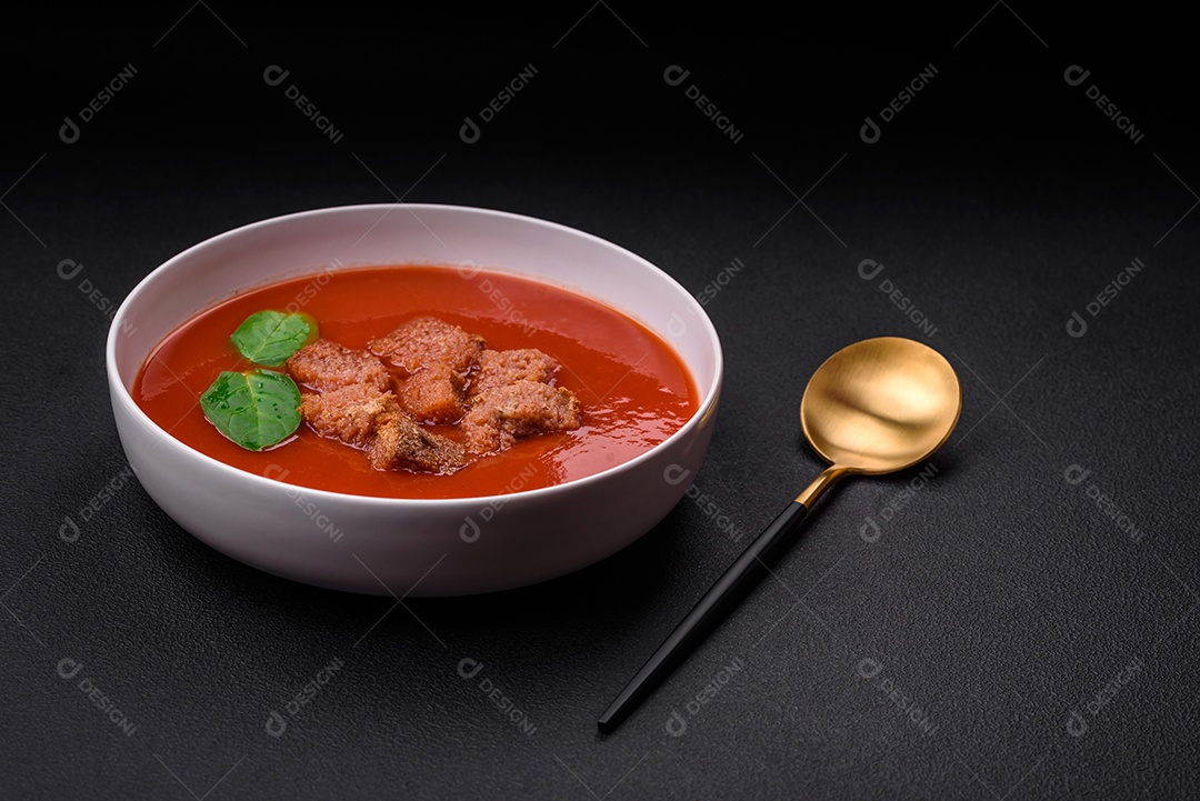 Delicioso gaspacho fresco com pão ralado, sal e especiarias numa placa cerâmica sobre um fundo escuro de concreto
