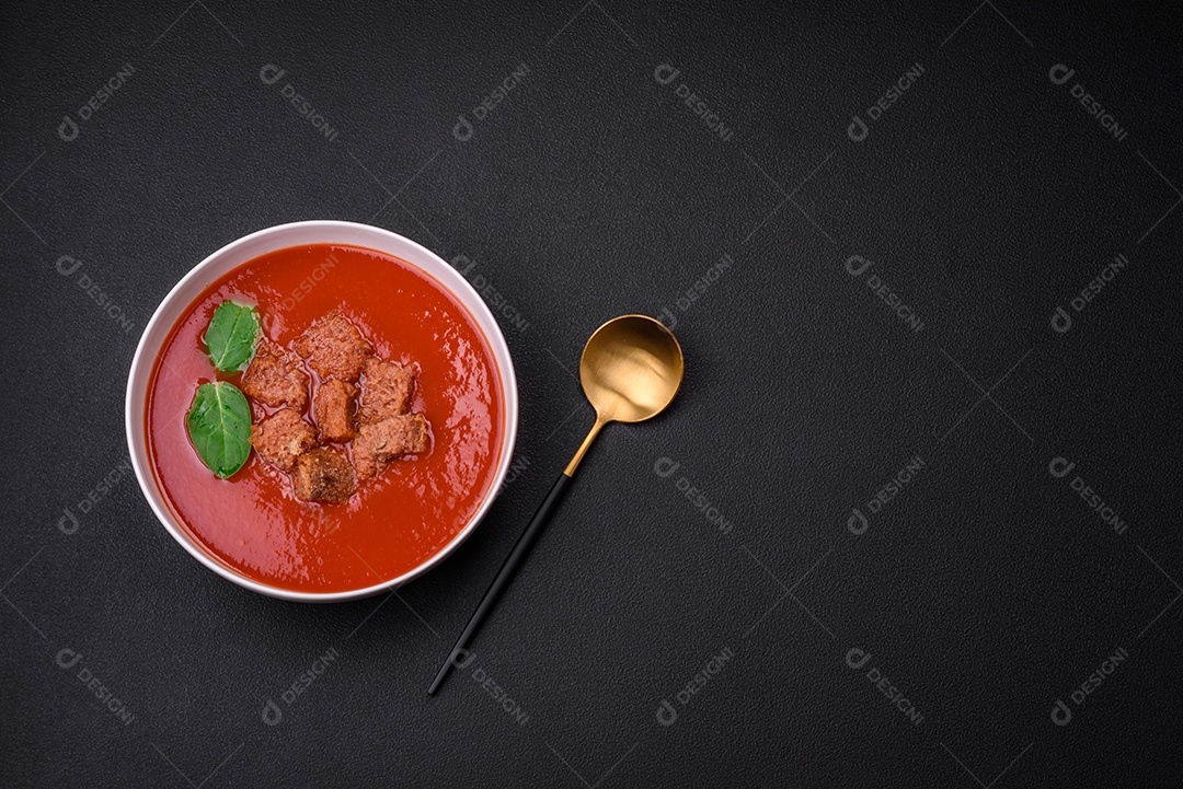 Delicioso gaspacho fresco com pão ralado, sal e especiarias numa placa cerâmica sobre um fundo escuro de concreto